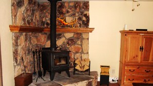 A stone fireplace with a black stove, a wooden cabinet, and a stone wall. - Relaxing, Spiritual, Meditative Residential House - Large yard!  MONTHLY RENTAL. (Sedona)