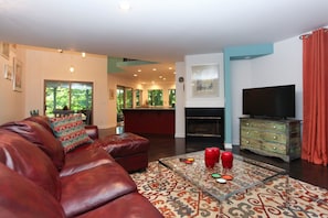 A living room with a leather couch, a glass coffee table with red cups, a television, and a fireplace.