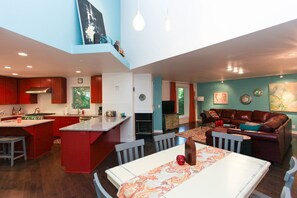 A spacious kitchen with a central island, a dining area with a patterned table runner, and a living room with a brown leather couch.