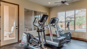 Un gimnasio en casa con cintas de correr y elípticas, ventanas amplias y un ventilador de techo.