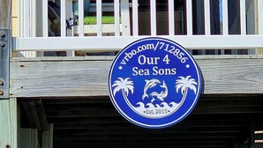 Een blauw bord met witte tekst met daarop 'Our 4 Sea Sons' en 'Est. 2015', bevestigd aan een houten constructie.