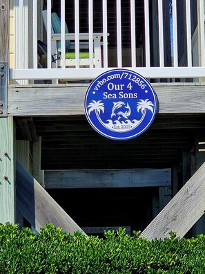 A blue sign with white text stating "Our 4 Sea Sons" and "Est. 2015" on a wooden structure.