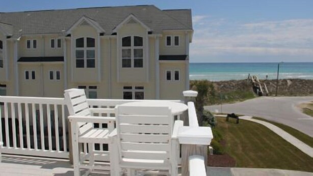 Een pand aan het strand met een wit gebouw, een balkon met witte stoelen en uitzicht op de oceaan.