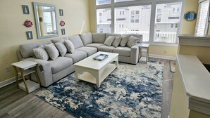 Een woonkamer met een grijze hoekbank, een witte salontafel en een blauw tapijt met patroon.