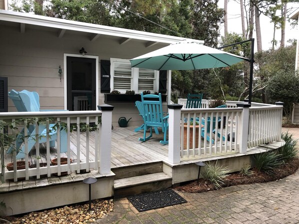 A covered porch with a white railing, blue chairs, and a green umbrella. - Few short steps from the beach (Grayton beach)