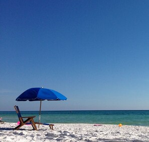 A beach with a blue umbrella, a wooden chair, and a sandy shore. - Few short steps from the beach (Grayton beach)