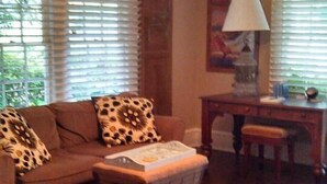 Una sala de estar con un sofá, una mesa de centro, un sillón estampado de leopardo, una lámpara y un ventilador de techo.