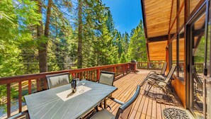 Eine Holzterrasse mit Tisch und Stühlen, umgeben von hohen Bäumen.