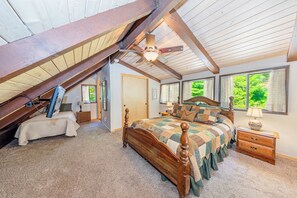 Une chambre avec un plafond en pente, un lit en bois, une table de chevet et une fenêtre donnant sur un paysage verdoyant.