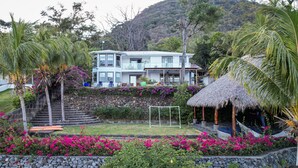 A two-story house with a stone staircase leading to the entrance, surrounded by lush greenery and vibrant flowers.