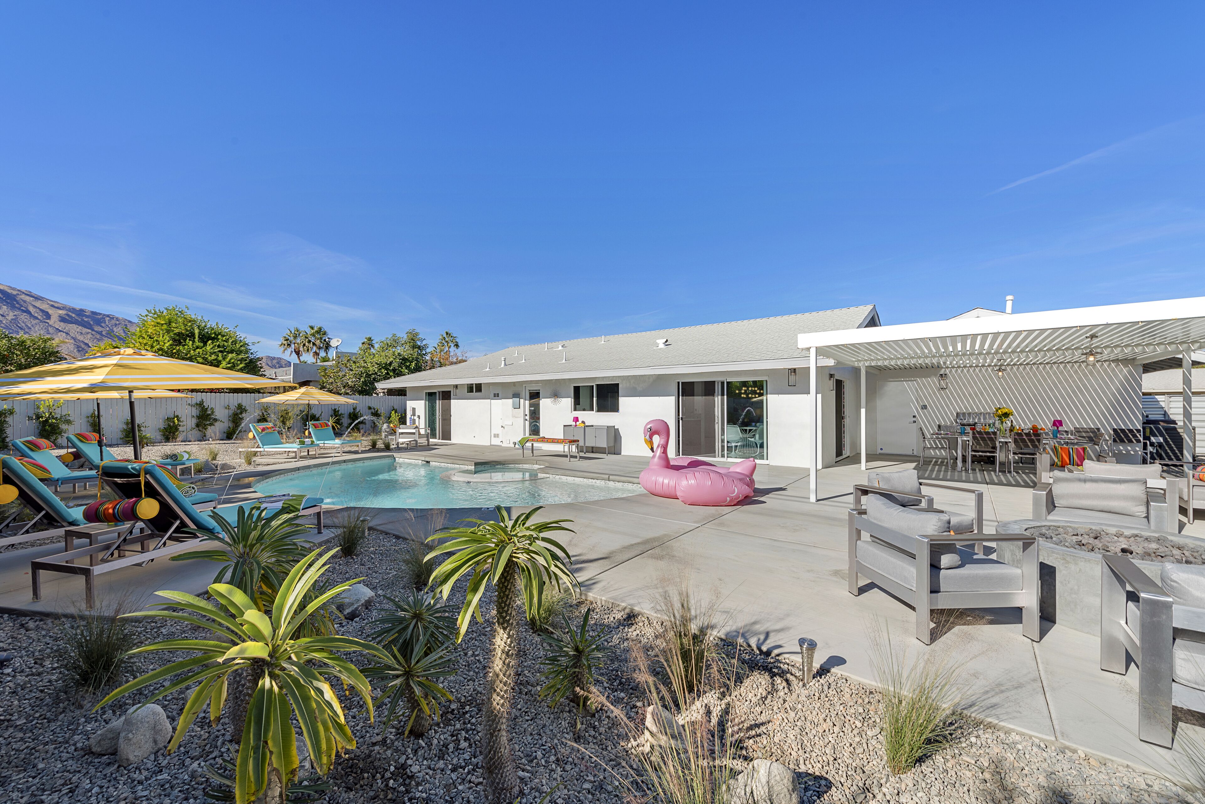 Ein moderner Poolbereich im Freien mit Liegestühlen, einem pinken Flamingo-Schwimmpfad und einer überdachten Terrasse.