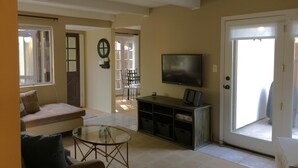 Una sala de estar con sofá, una mesa de centro de vidrio, televisor y puerta corrediza de vidrio que da a un patio.