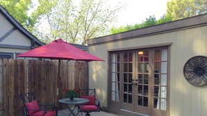 Un patio con cerca de madera, una mesa con dos sillas y un paraguas rojo.