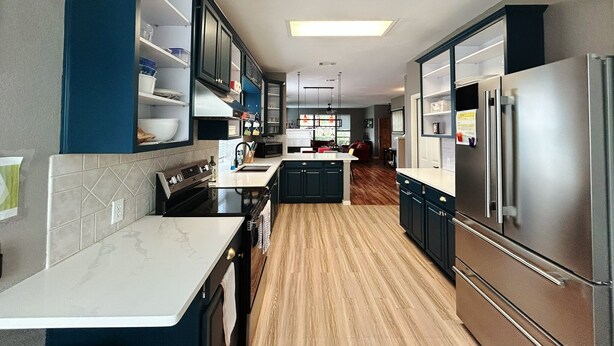 A modern kitchen with dark cabinets, a stainless steel refrigerator, and a wooden floor. - 4BR/4BA Quiet Central Frisco Home - Near Star Center, UNT, Toyota Sta. + Hot Tub (Frisco)