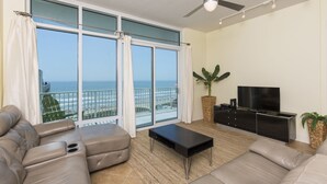Un soggiorno moderno con un'ampia finestra vista oceano, una ventola a soffitto e un televisore a schermo piatto su un mobile nero.