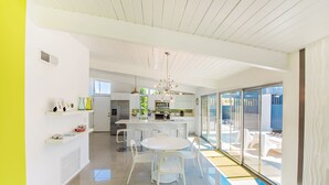 A modern kitchen with white cabinetry, a central island, and a dining area with white chairs. - Beautiful! Remodeled Mid-Century Alexander w/ SALTWATER pool, spa, bikes, & more (Palm Springs)