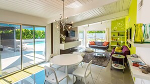 A modern living room with a dining area, a fireplace, and a pool view. - Beautiful! Remodeled Mid-Century Alexander w/ SALTWATER pool, spa, bikes, & more (Palm Springs)
