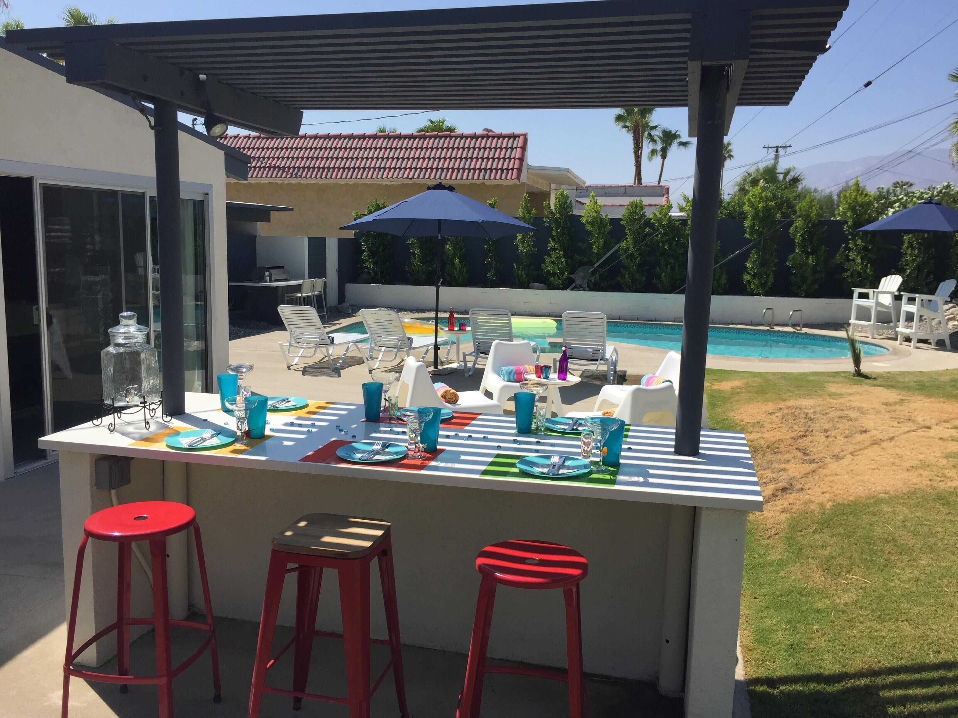 Un espace extérieur abrité où l’on peut prendre ses repas, avec une piscine en arrière-plan.