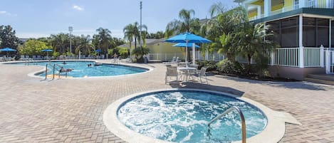A pool area with two hot tubs, lounge chairs, and umbrellas.
