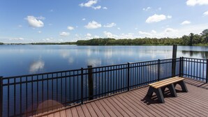 Une terrasse en bois avec un banc donnant sur un lac paisible, le tout entouré d’une rambarde en métal.