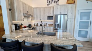 Een moderne keuken met granieten aanrechtbladen, roestvrijstalen apparatuur en een centraal eiland met barkrukken.