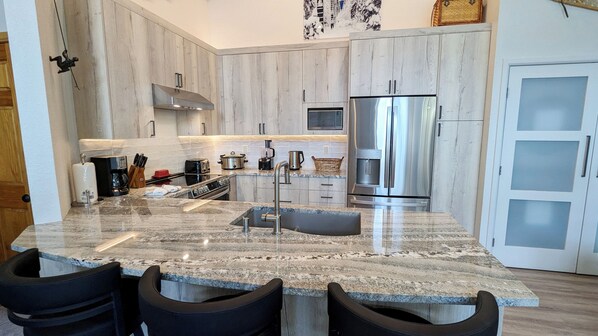 A modern kitchen with granite countertops, stainless steel appliances, and a central island with bar stools.