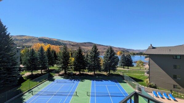 A tennis court with a net, surrounded by trees and a lake view.
