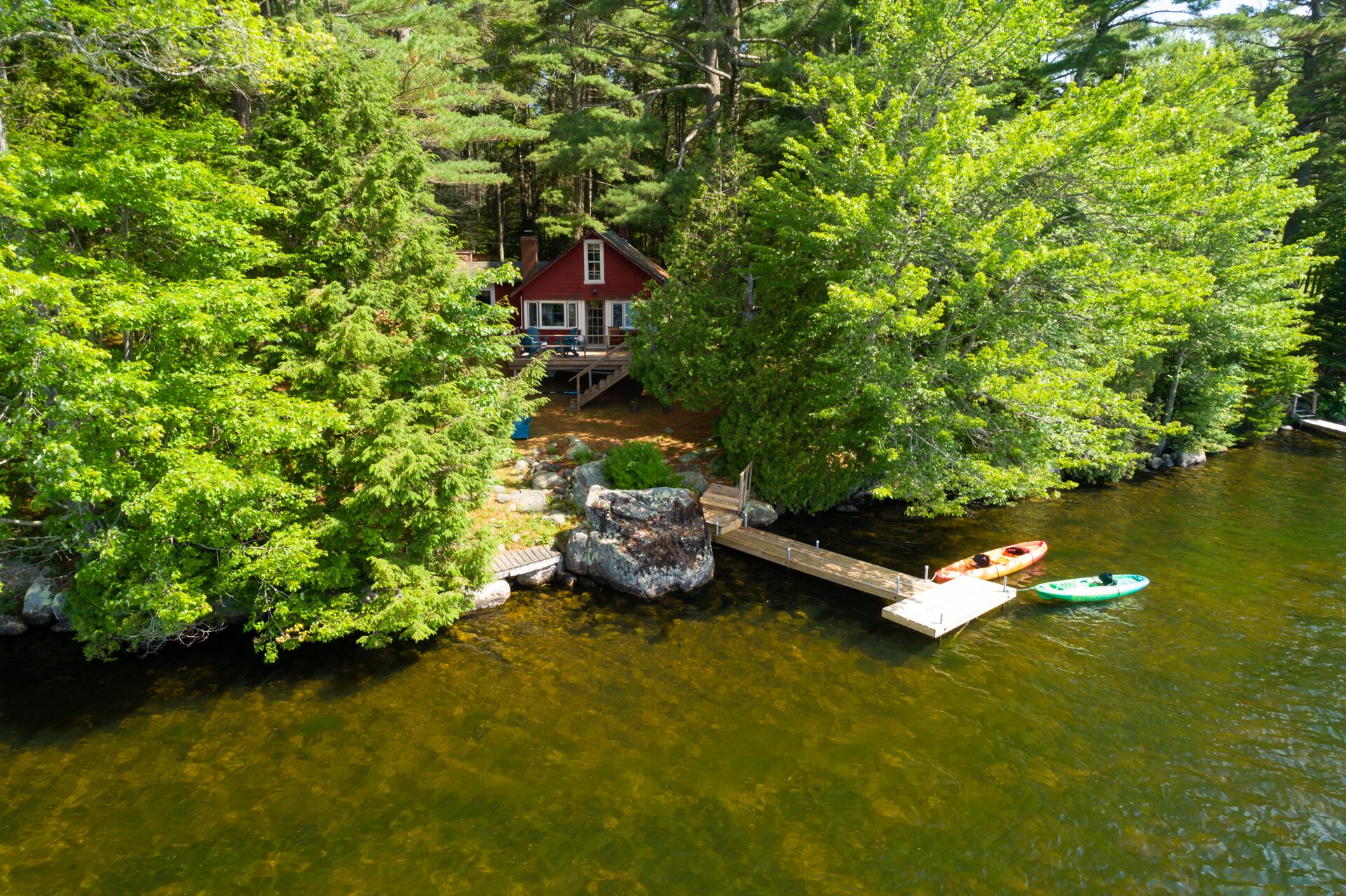 A house surrounded by dense forest, a dock extending into a river, and a kayak on the water.