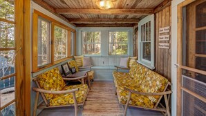 A cozy wooden cabin with a porch, wooden furniture, and framed pictures.