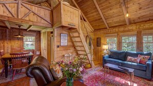 A rustic cabin interior with a dining area, a sofa, a coffee table, and a staircase.
