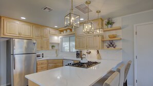 Una cocina moderna con una isla grande, electrodomésticos de acero inoxidable, armarios de madera e iluminación colgante.