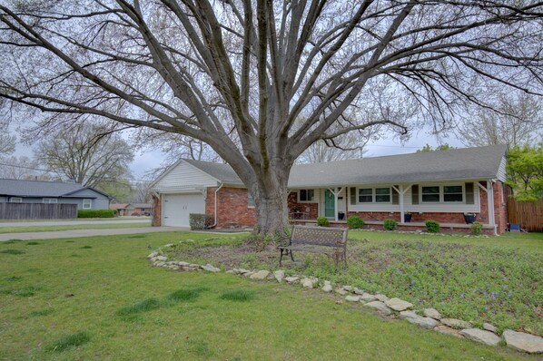 A residential house with a large tree in the front yard, a front porch, and a small garden area.