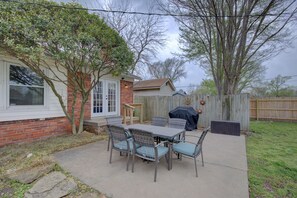 A backyard with a patio table and chairs, a barbecue grill, and a wooden fence.