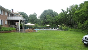 Une cour arrière verdoyante avec une piscine, des tables de pique-nique et des parasols.