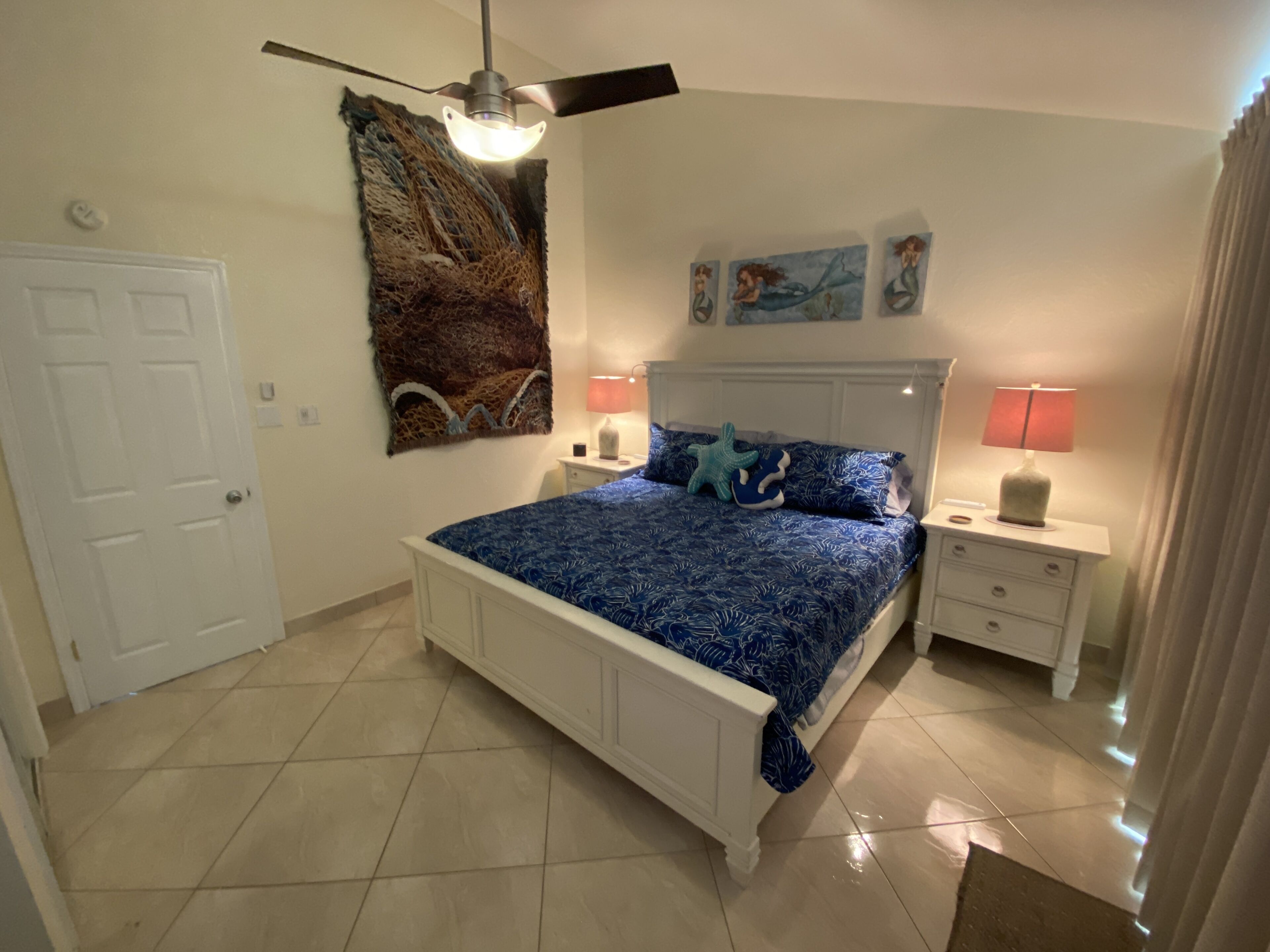 Ein Schlafzimmer mit einem Bett, zwei Nachttischen, einem Deckenventilator und Bildern an der Wand.