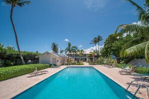 A rectangular swimming pool with a clear blue water surface, surrounded by a paved deck with lounge chairs and palm trees. - Seven Mile Beach, Cayman Grand 32, 2 bd/2bth condo w/pool at Island Pine Villas (Seven Mile Beach)