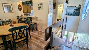 Un comedor con mesas y sillas de madera, una cocina al fondo y una escalera que sube a un nivel superior.