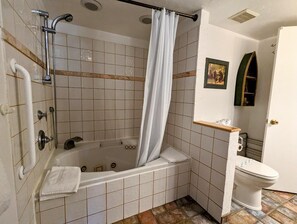 A bathroom with a bathtub, shower, toilet, and a small shelf with toiletries.