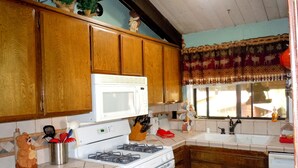 Una cocina con armarios de madera, estufa blanca, microondas y ventana con cortina estampada.