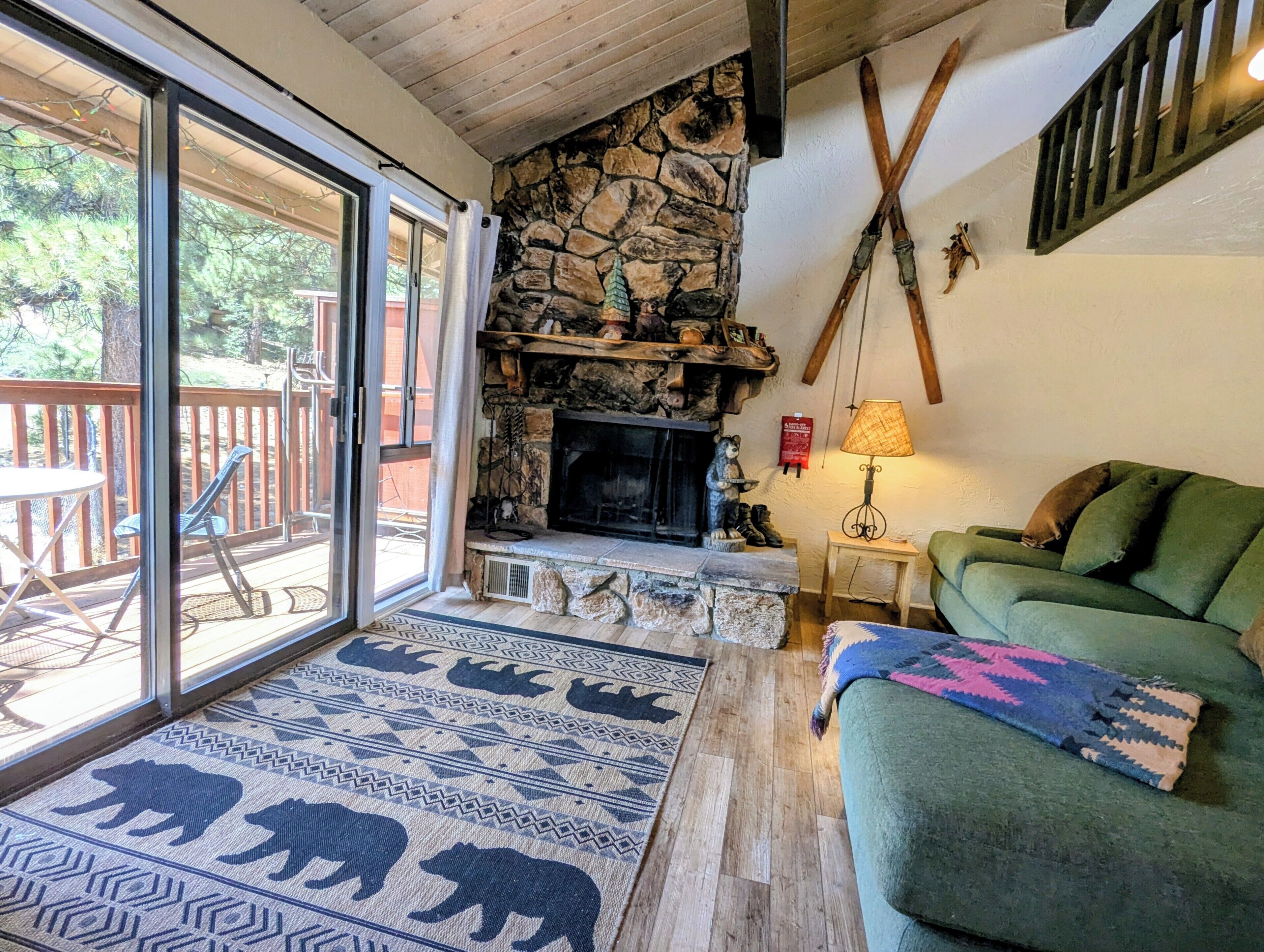 A cozy living room with a stone fireplace, a green sofa, and a patterned rug.