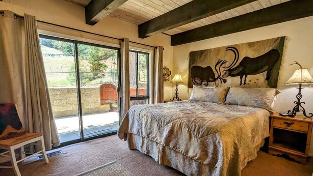 Un dormitorio con una cama grande, una ventana con cortinas, un cuadro de una vaca y una mesita de noche con una lámpara.