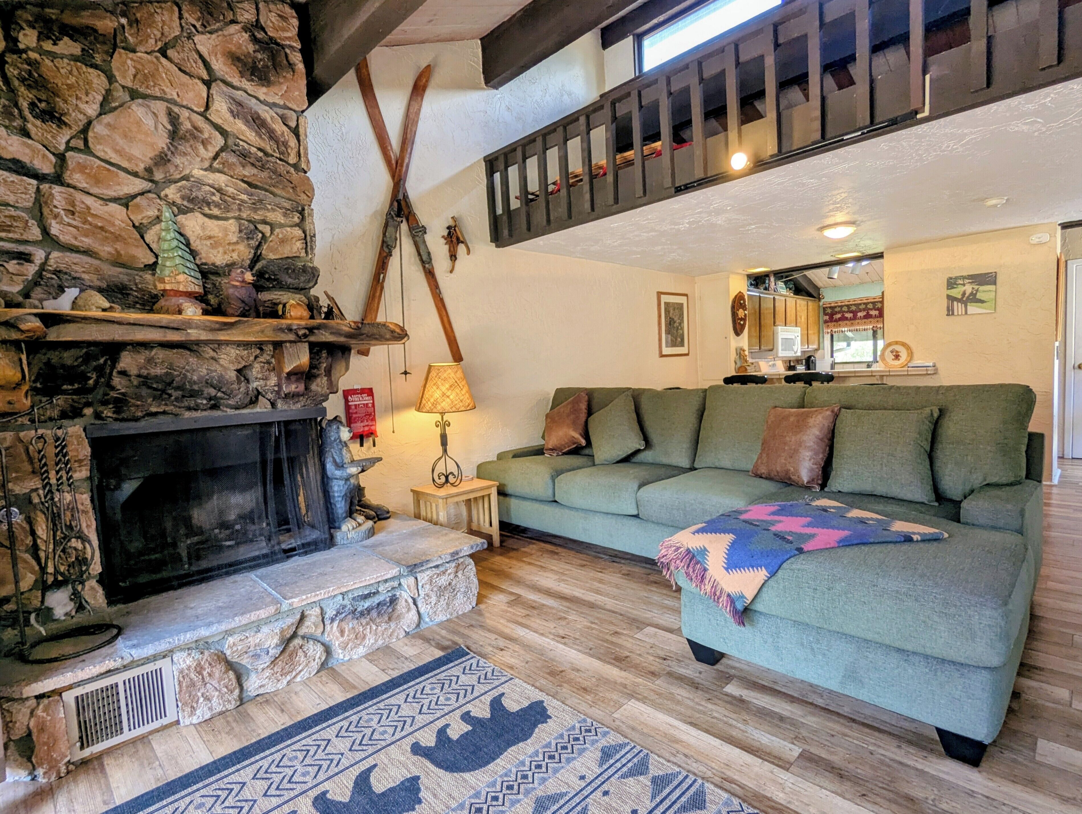 A cozy living room with a stone fireplace, a green sofa, and a wooden floor.