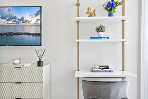 Un intérieur moderne avec une console blanche, une bibliothèque remplie de livres, une plante décorative et un tableau encadré accroché au mur.