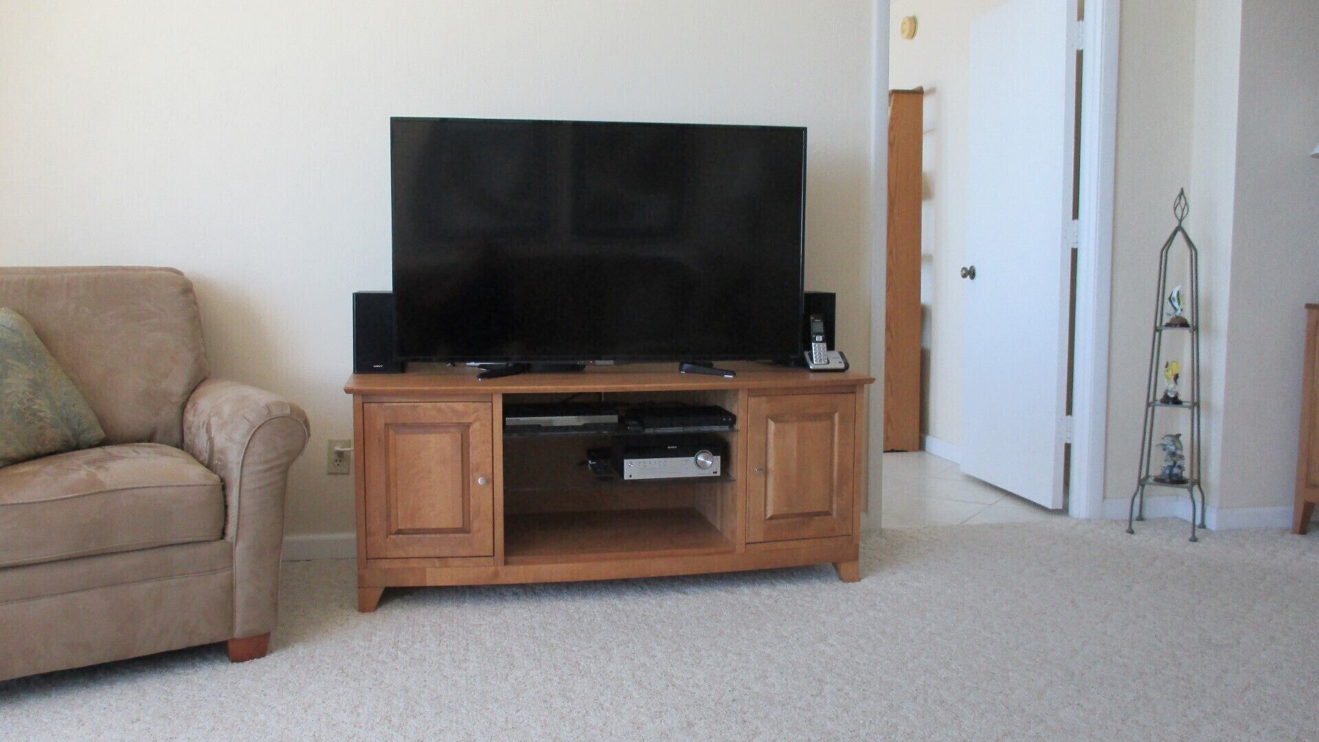 Een woonkamer met een beige bank, een houten tv-meubel en een klein kastje.