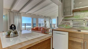 A modern kitchen with a view of the ocean, a dining area with a sofa, and a kitchen island.