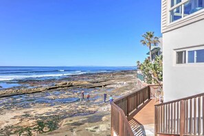 Vista costeira com deck de madeira, com vista para uma praia rochosa e oceano.