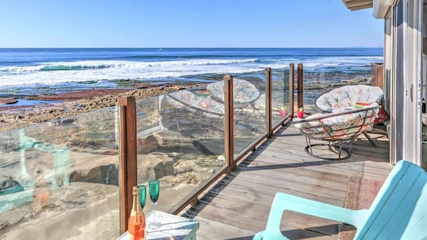 A wooden deck with a glass railing overlooking a rocky beach and ocean.