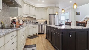 A modern kitchen with white cabinets, a stainless steel refrigerator, and a large island. - Tons of Space & Gorgeous Porch! (Savannah)
