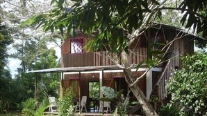 Ein zweigeschossiges Holzhaus mit einem Balkon, umgeben von üppiger Vegetation.