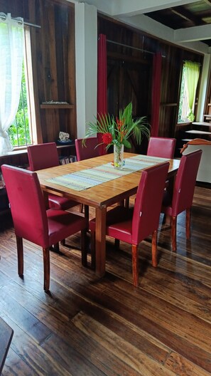 Une table à manger en bois, des chaises rouges, un vase avec des fleurs et un plancher en bois.